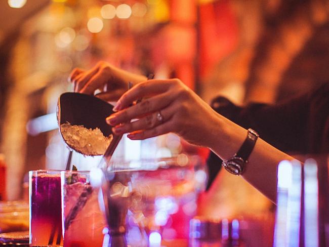 Midsection of a young female bartender preparing a cocktails in a nightlife cocktail bar. Selective focus. Focus on foreground.