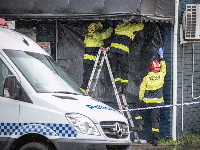 Emergency services workers cover the martial arts centre with black plastic. Picture: Julian Andrews