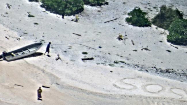 In this August 25, 2016, photo provided by the U.S. Navy, a pair of stranded mariners signal for help as a U.S. Navy P-8A Poseidon aircraft crew from Patrol Squadron (VP) 8 flies over in support of a Coast Guard search and rescue mission on an uninhabited island in Micronesia, Hawaii. The U.S. Coast Guard says the two stranded mariners were rescued Friday after crews saw their “SOS” in the sand. Picture: US Navy via AP