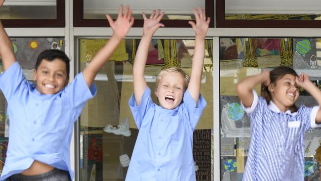 Excited school children with arms in the air and proud school teacher smiling