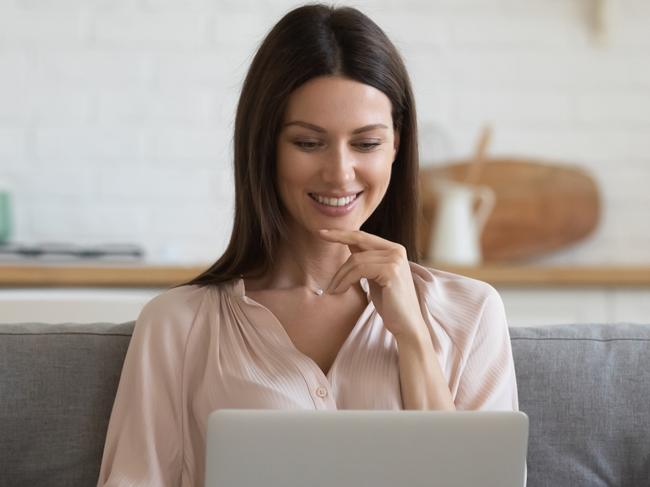 Smiling young woman using a computer, sitting on couch at home, beautiful girl shopping or chatting online in social network, having fun, watching movie, freelancer working on computer project or filing her tax.  Source: iStock.