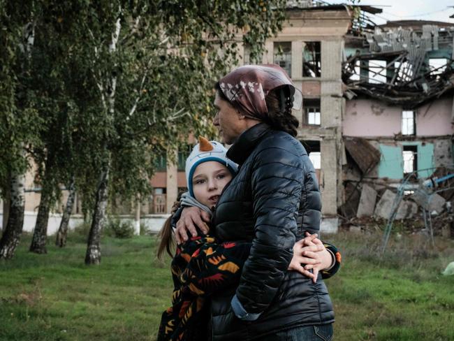 Olga Srednyakova (R), 51, a single mother of the eight children, hugs the youngest daughter Vera, 8, as other ones harvest mushrooms at an abandoned ground of their destroyed school in Konstantinovka in the Donetsk region on October 13, 2022, amid the Russian invasion of Ukraine. (Photo by Yasuyoshi CHIBA / AFP)