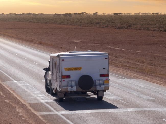 An Australian Outback touring caravan on the road in the early morning near Eucla, on the Western/South Australia border. The markings on the road show it is a Flying Doctor landing strip.