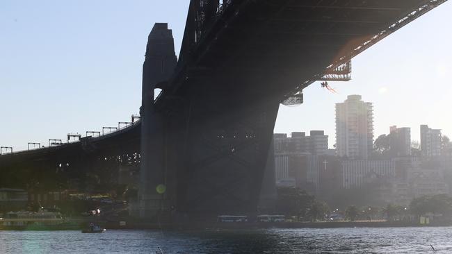 Three protesters are pictured hanging from the bridge holding orange ribbons. Picture: Richard Dobson