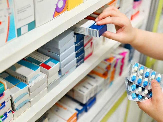 Pharmacist holding medicine box and capsule pack in pharmacy drugstore.