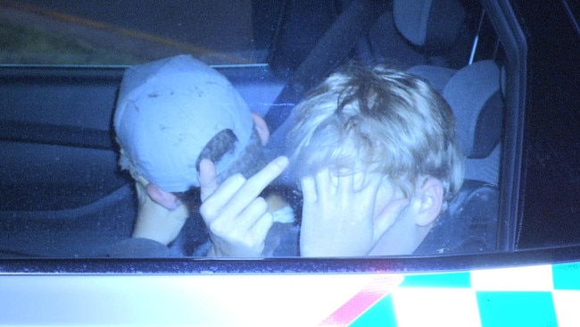 A boy sticks his middle finger up from the back of a police car after a Kia Sportage alleged to be stolen struck a Ford Falcon ute in 2021.