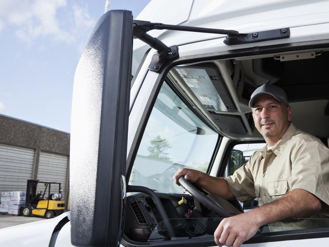 Truck driver (30s) sitting in cab of semi-truck.