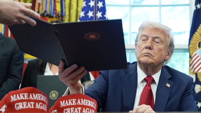 President Donald Trump is handed an executive order to sign in the White House.