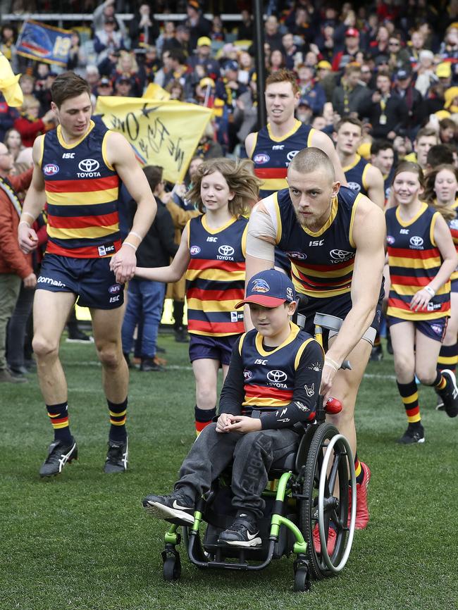 Hugh Greenwood pushes a wheelchair-bound Crows mascot as the team runs out against North Melbourne. Picture: Sarah Reed