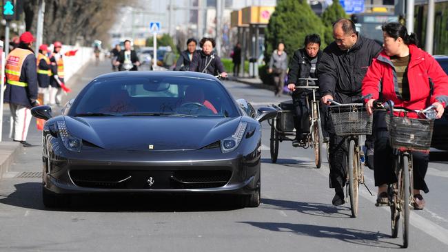 Cyclists ride past an illegally parked Ferrari on a main road in Beijing, China. Picture: AFP