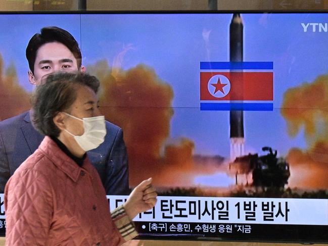 TOPSHOT - A woman walks past a television showing a news broadcast with a file photo of a North Korean missile test, at a railway station in Seoul on November 17, 2022. (Photo by Anthony WALLACE / AFP)