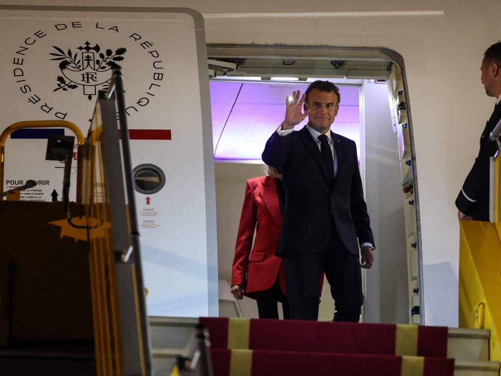 Emmanuel Macron waves in front of his wife Brigitte Macron as they prepare to make their way down the plane’s steps after the shoving incident. Picture: AFP