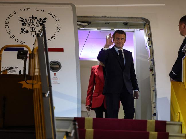Emmanuel Macron waves in front of his wife Brigitte Macron as they prepare to make their way down the plane’s steps after the shoving incident. Picture: AFP