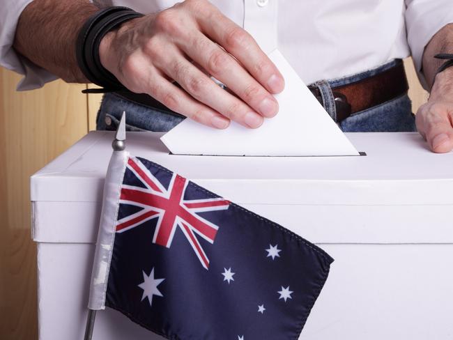 A man inserting a ballot to a ballot box.  Australian flag in front of it.