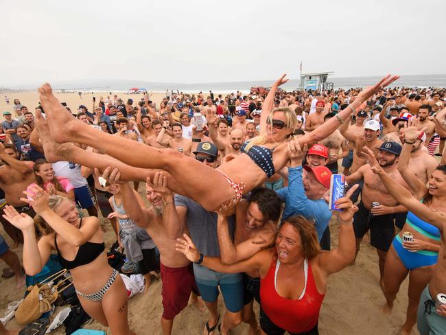 Repeat female champion Annie Seawright-Newton is lifted into the air after winning the 47th annual Hermosa Beach Ironman competition where participants must run a mile, paddle a surfboard a mile, and chug a six-pack of beer on July 4, 2021 in Hermosa Beach, California. - The unconventional triathlon held for over 40 years returns for the Fourth of July holiday after being cancelled last year due to the Covid-19 pandemic. Competitors run a mile, paddle a surfboard a mile, and chug a six pack of beer - those who puke their beer up are disqualified but some intentionally vomit to see who can puke the best. (Photo by Patrick T. FALLON / AFP)