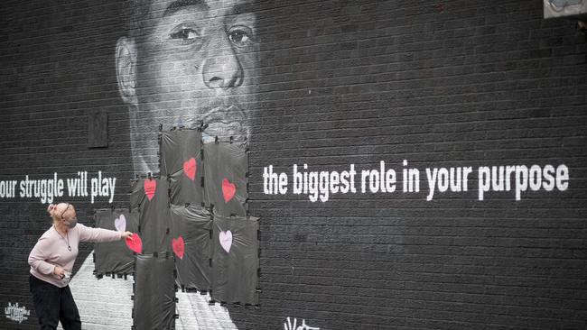 An English fan covers offensive graffiti with hearts on a Marcus Rashford mural.