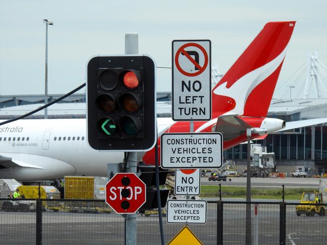 Road signs and traffic lights at the corner of Nigel Love Bridge and Airport Drive, Mascot.  In the background is a Qantas Airbus A330-202 plane, registration VH-EBN, parked on the tarmac of Sydney Kingsford-Smith Airport. In the distance is the domestic terminal.  This image was taken from Nigel Love Bridge, Mascot on a cloudy afternoon on 2 December 2023. Aircraft generic.