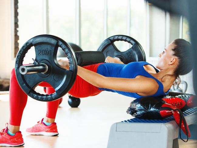 Glutes. Closeup side view of an attractive mid 20's brunette performing hip thrust exercise with a weighted barbell.