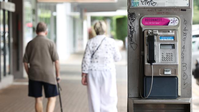 People walk past a public pay phone covered in graffiti tags on Abbott Street in the Cairns CBD. Picture: Brendan Radke