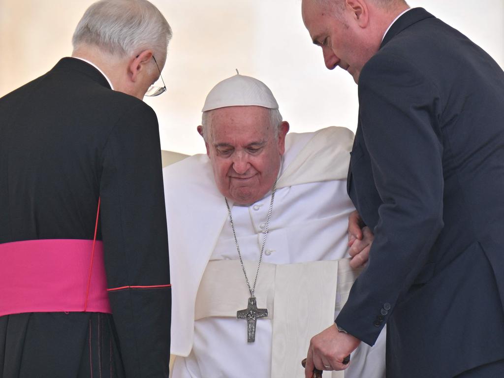 Prefect of the Pontifical House, Monsignor Leonardo Sapienza, left and an aide, right, help Pope Francis get up from his chair. Picture: AFP