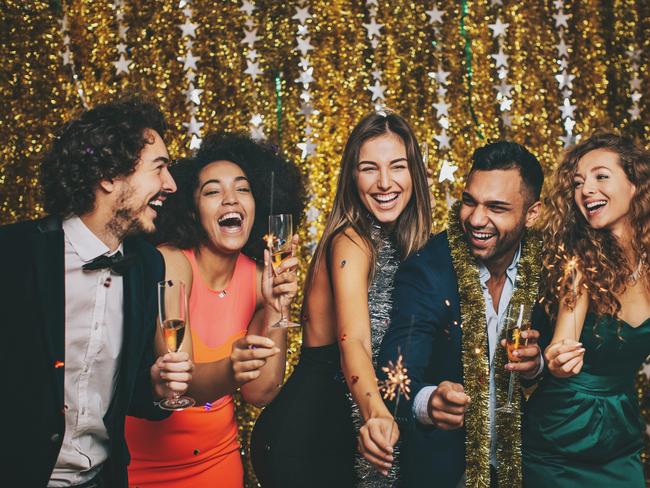 Multi-Ethnic group of cheerful people in formal wear holding chanpagne glasses and sparklers at New Year's celebration.