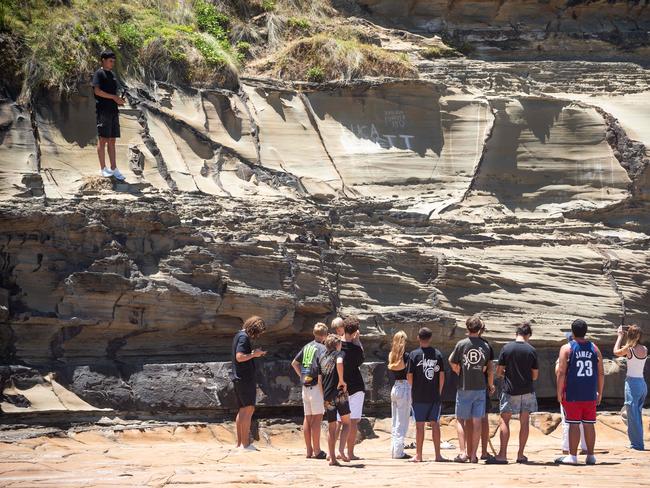 Friends of Luca Bennett scratch his name into the rock at North Avoca where he was swept off yesterday afternoon. Picture: Tom Parrish