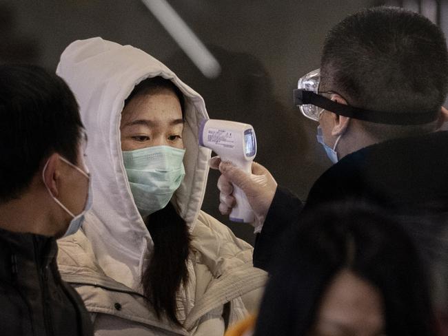 A Chinese passenger on the last bullet train from Wuhan to Beijing is checked for a fever by a health worker at a Beijing railway station. Picture: Kevin Frayer/Getty