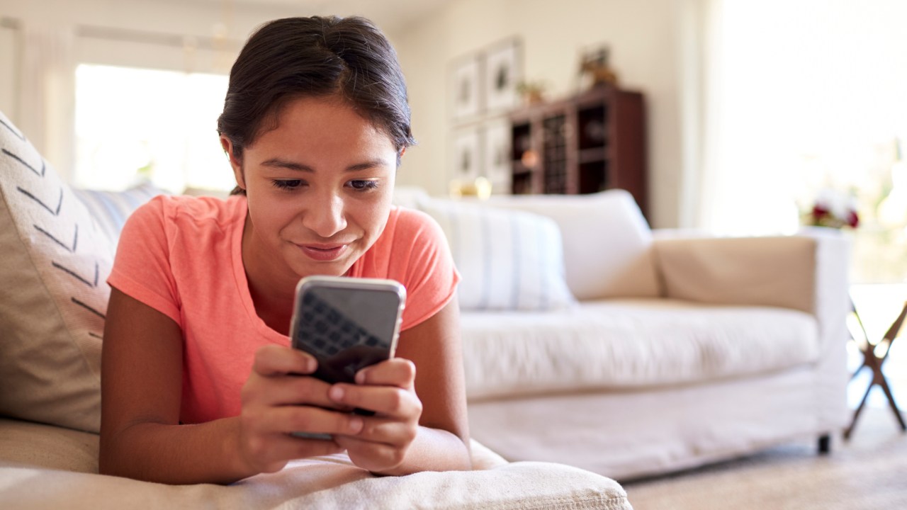 Teenage girl lying on the sofa at home in the living room using smartphone, close up, low angle, close up