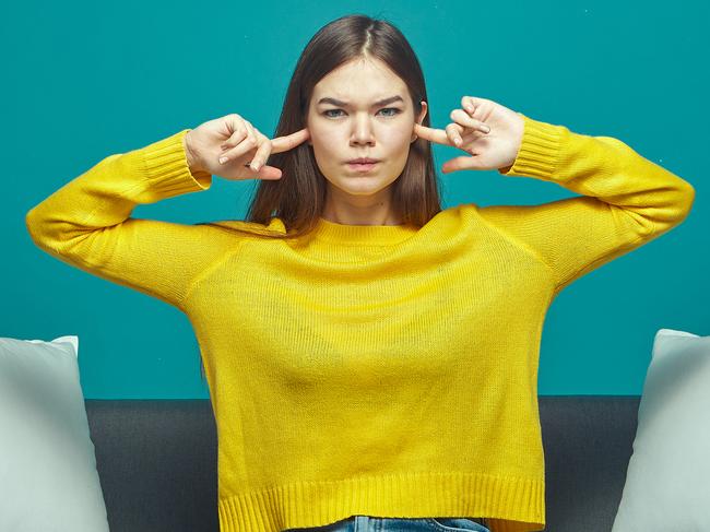 Irritated young girl close, plug ears, ignoring loud sound or noise, sitting on sofa, annoyed by noisy neighbors. High quality photo