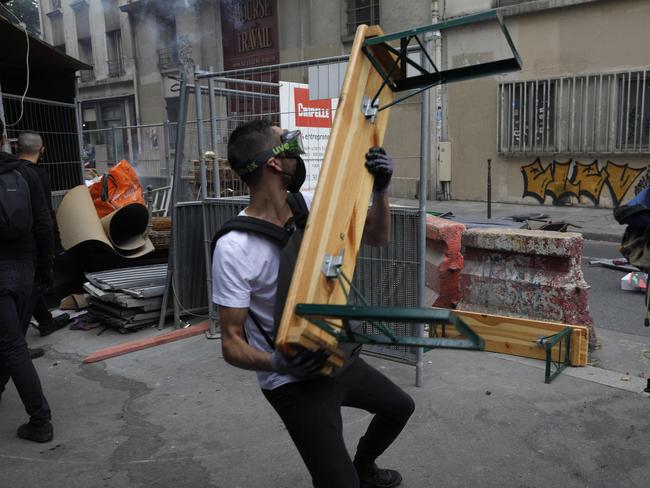 A protestor throws a wooden bench during a demonstration, part of a national day of protest against French legislation making a Covid-19 health pass compulsory to visit a cafe, board a plane or travel on an inter-city train, in Paris on July 31, 2021. - The legislation passed by parliament the week before has sparked mass protests in France but the government is determined to press ahead and make the health pass a key part of the fight against Covid-19. A valid health pass is generated by two jabs from a recognised vaccine, a negative coronavirus test or a recent recovery from infection. The legislation also makes vaccination compulsory for health-workers and carers. The pass has already been obligatory from July 21 for visits to museums, cinemas and cultural venues with a capacity of more than 50 people. (Photo by GEOFFROY VAN DER HASSELT / AFP)