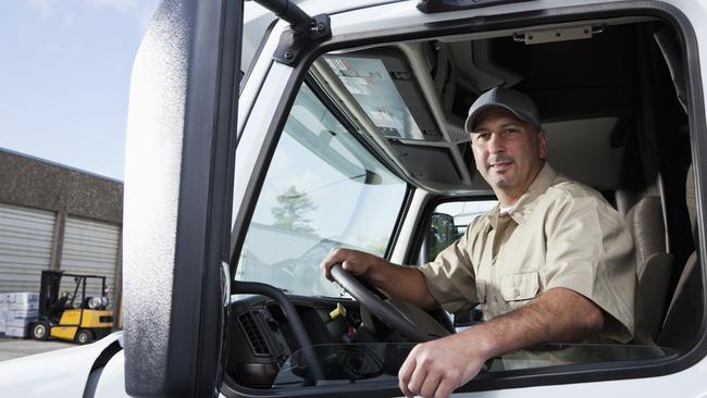 Truck driver (30s) sitting in cab of semi-truck.