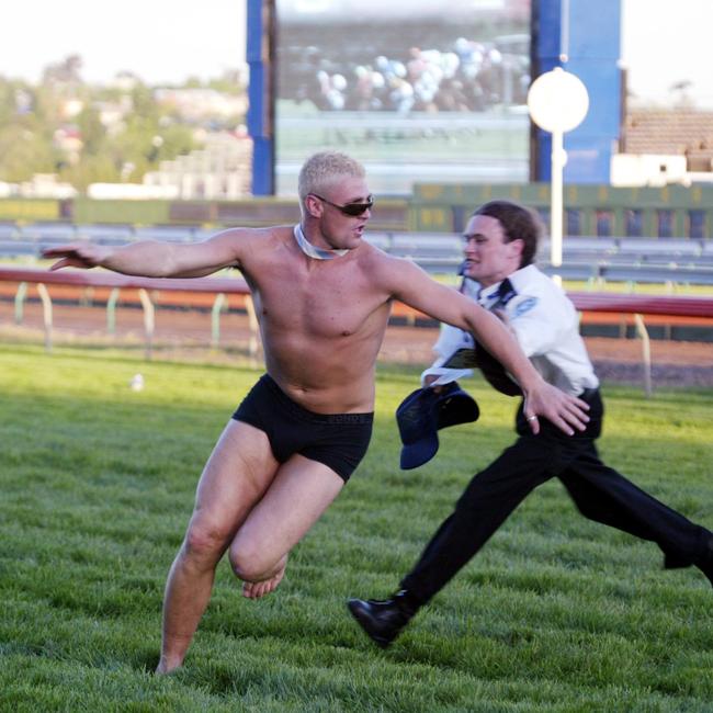 A bloke struggles to get to the line as he evades a security guard after the last race at Derby Day 2004.