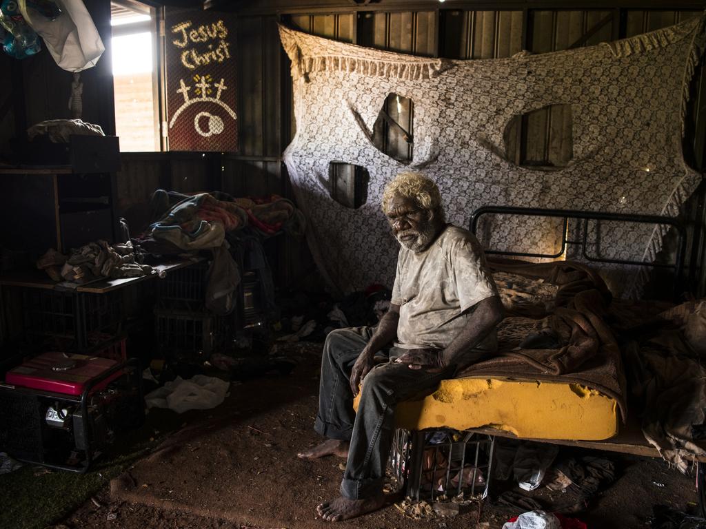 Steven Camfoo, 58, sits in the tin house he calls home in Drive-in Camp, named after the long-since-shuttered drive-in cinema nearby, in Tennant Creek. Camfoo has lived here for about ten years, despite being disconnected from water, electricity and rubbish collection services, because of a housing shortage. His and other tin sheds still inhabited by long-term residents are leaky in the rain, cold in the winter and scorching hot in the summer. Camfoo collects water in plastic containers pushed in a baby stroller. Picture: Andrew Quilty | See more Andrew Quilty pictures in The Weekend Australian Magazine story on the remote housing crisis