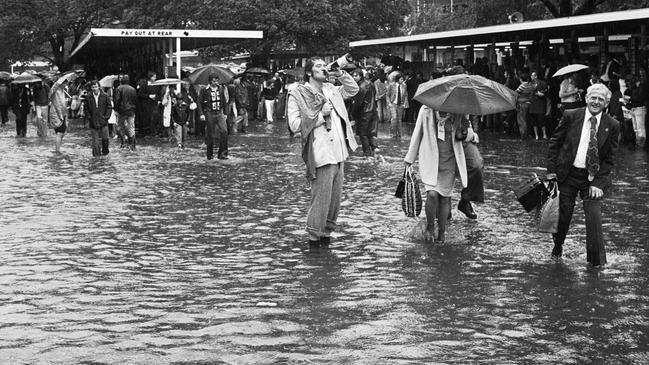 A punter drinks champagne from the bottle on a flooded betting ring in 1976.