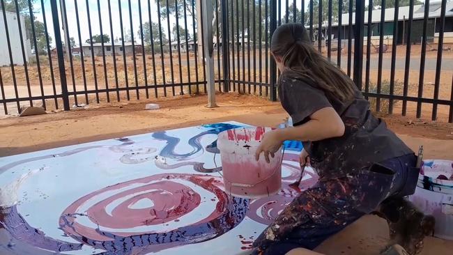 A non-Indigenous employee is seen contributing to a painting by (Indigenous) artist Yaritji Young.