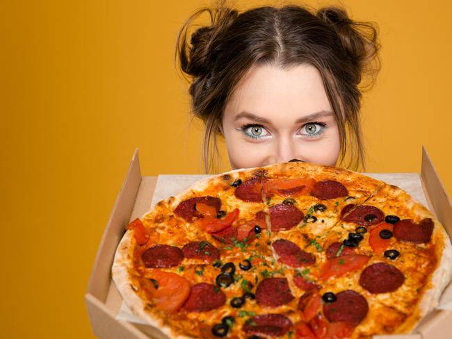 Lovely cute positive young woman hiding behind pizza over yellow background. Picture istock