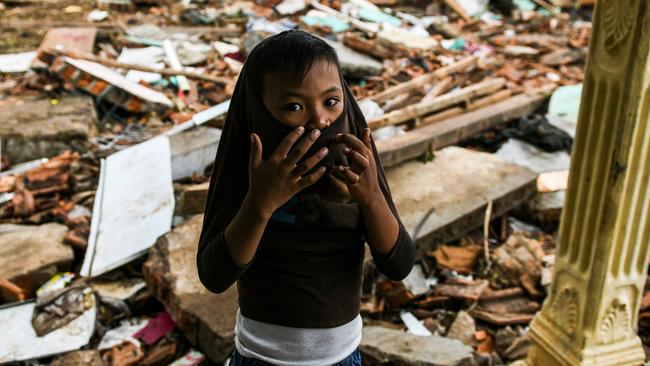 A boy covers his face as he stands outside a collapsed house in Rajabasa in Lampung province on December 25, 2018, three days after a tsunami - caused by activity at a volcano known as the "child" of Krakatoa - hit the west coast of Indonesia's Java island. - Desperately needed aid flowed into a stretch of Indonesia's tsunami-struck coastline on December 25, officials said, but aid workers warned that clean water and medicine supplies were dwindling as thousands crammed makeshift evacuation centres. (Photo by MOHD RASFAN / AFP)