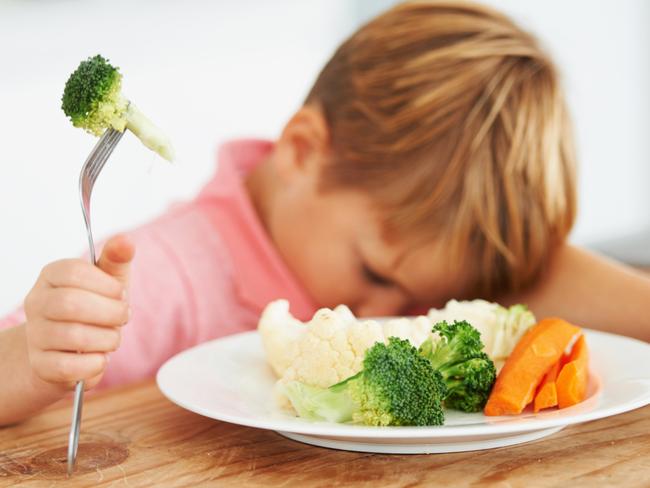 A cute young boy with his head on the table while holding a piece of broccoli on his fork. Picture: iStock