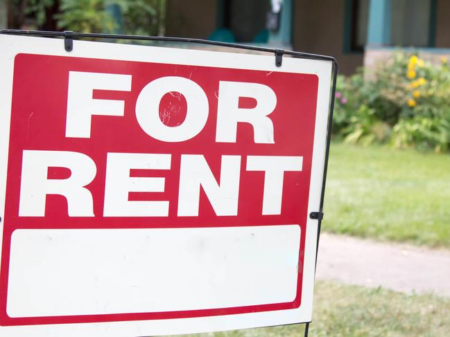 A blank red and white for rent sign is posted in the front yard of a home. The home has a porch and is a rental property.