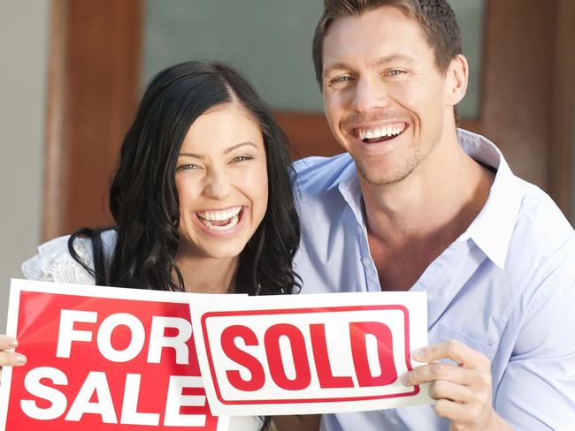 Happy couple holding for sale and sold signs in front of a new house