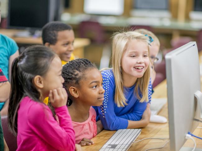 A multi-ethnic group of elementary age children are sitting in the computer lab and are using the computers to play a game together.