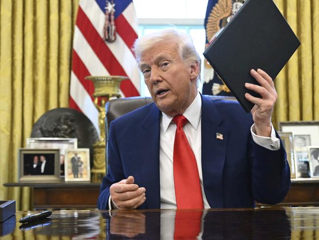 President Donald Trump holds an executive order in the Oval Office of the White House Wednesday, April 9, 2025, in Washington. (Pool via AP)