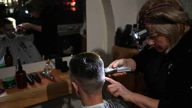 A hairdresser works with a headlamp during a partial blackout in Lviv on November 28, 2024, following Russian strikes on Ukrainian energy infrastructure, amid the Russian invasion of Ukraine. Russia's army on November 28, 2024 launched a massive attack on Ukraine's energy sector, forcing emergency power outages as temperatures dropped to freezing across the country. (Photo by YURIY DYACHYSHYN / AFP)