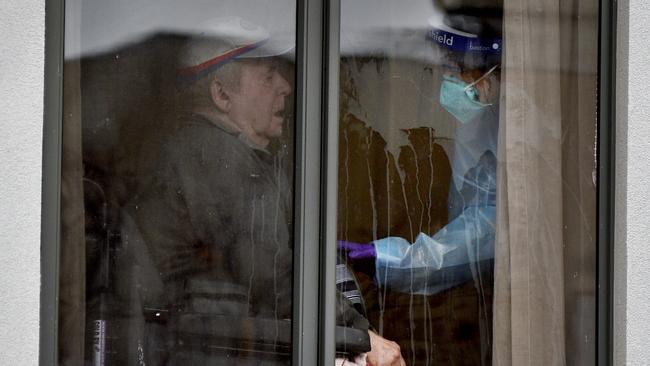 A resident at the locked-down Arcare Maidstone Aged Care in Melbourne's west is attended to by a medical staff member on Tuesday. Picture: Andrew Henshaw