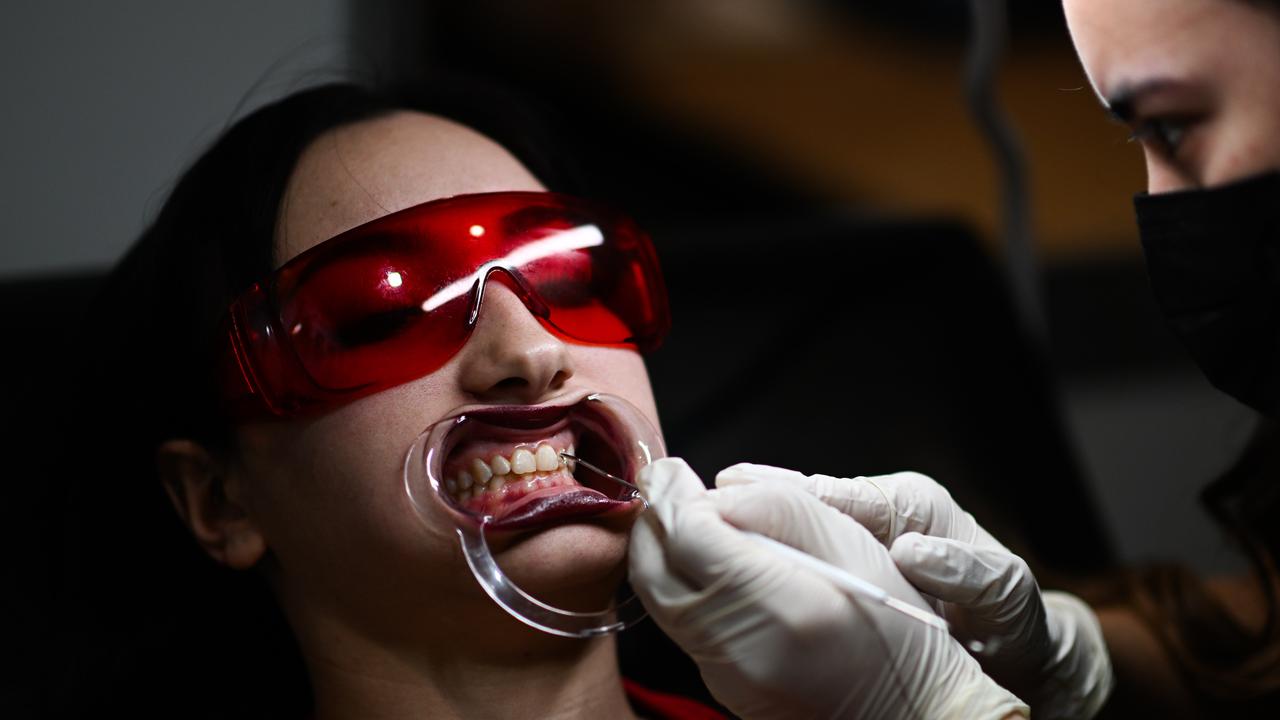 A woman gets her teeth inked by a tattoo artist. Picture: Dan Peled / NewsWire