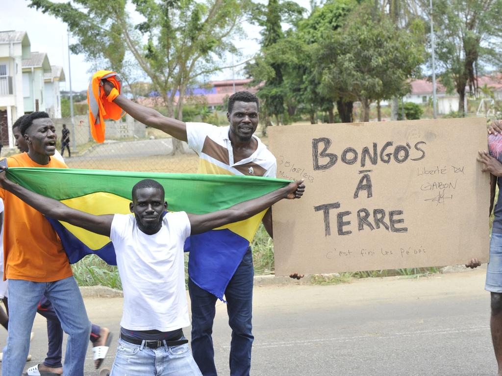 Residents celebrating next to a post that says Bongo’s a Terre which can be roughly translated to Bongo’s down. (Photo by AFP)