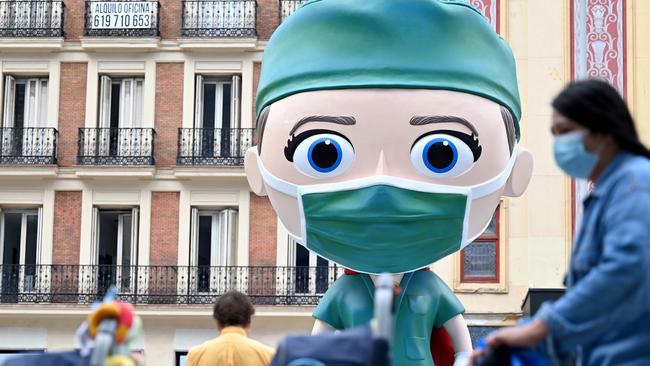 People wearing face masks walk on September 24, 2020 by a 6 meters high statue depecting a "Superhealthworker"  installed in Madrid to pay tribute to the heroes who fight against coronavirus. (Photo by Gabriel BOUYS / AFP)