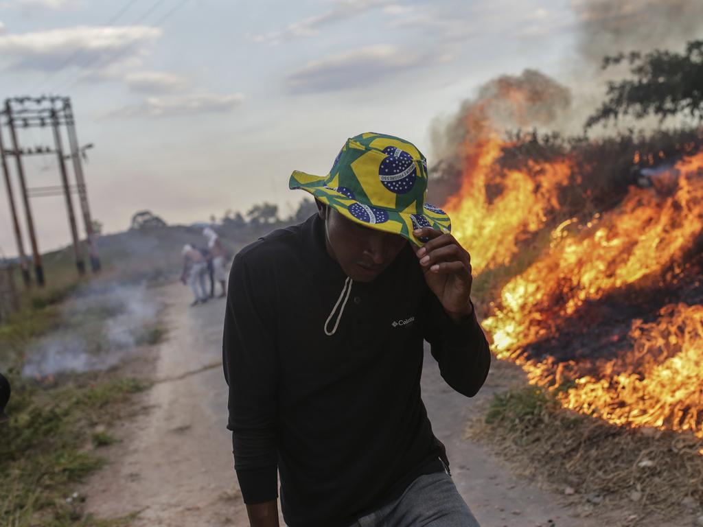 A man covers his face with a cap as he walks past a fire during a protest at the border between Brazil and Venezuela. Picture: AP