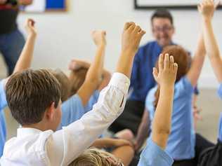 Excited school children in school uniform with hands up ready to answer a question from the teacher