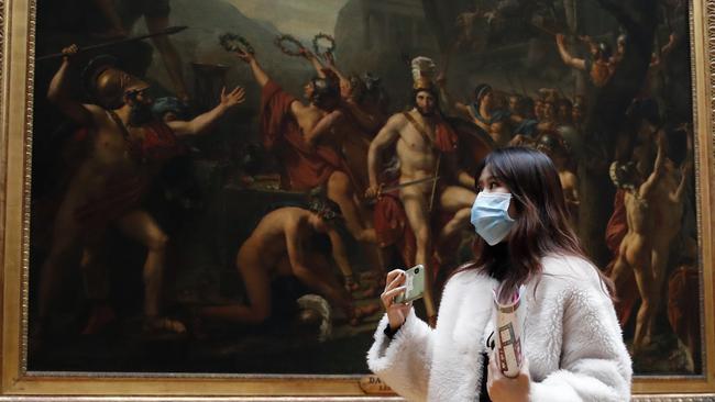 Masked tourist walks by an oil on canvas at the Louvre Museum in Paris.